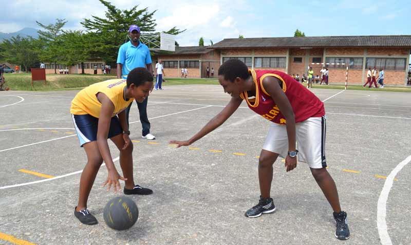 Ange tries to dribble past an opponent during practice at SOS HG Secondary School in Bujumbura, as the coach (in the background) looks on.