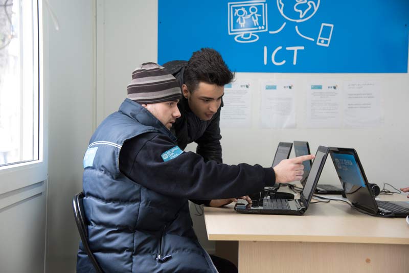 SOS staff with a refugee youth working on a laptop